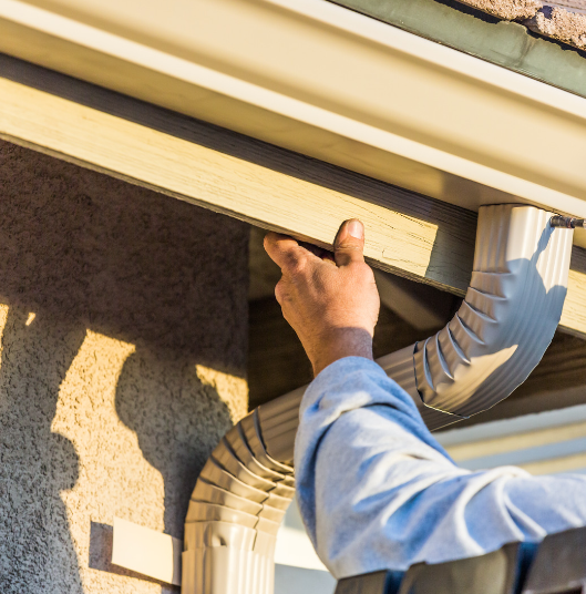 Hand holding a board and repairing home gutters.